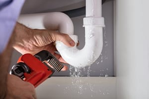 plumber with wrench fixing a plumbing leak